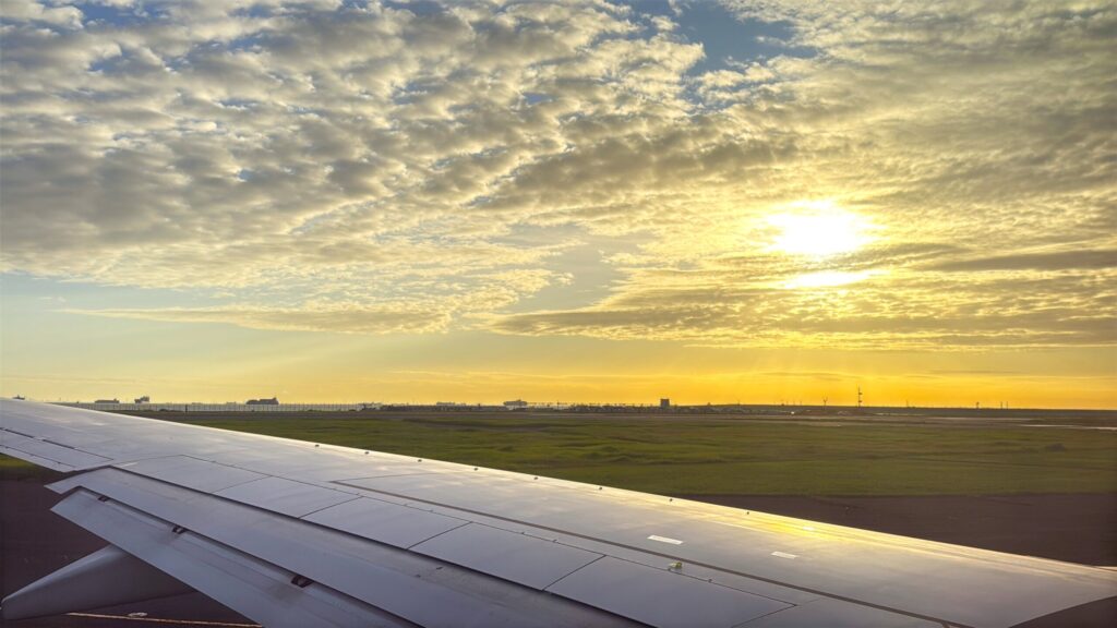 機内の窓からみた朝日と翼