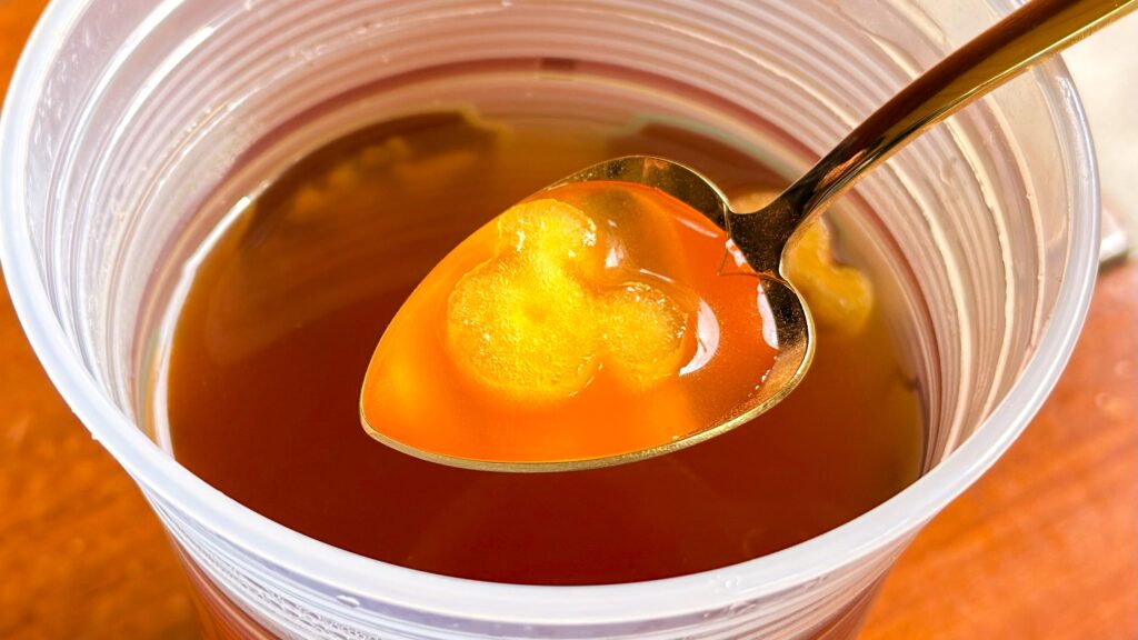 ディズニーリゾート_「ホットアップルジンジャードリンク」のミッキー型アップルをスプーンですくっている様子