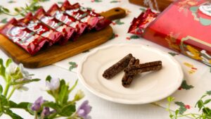 東京ディズニーリゾート_チョコレート風味「チュロススナック 紙箱 ミッキーマウスと仲間たち ディズニー・クリスマス」の皿盛りとパッケージが並んでいる様子