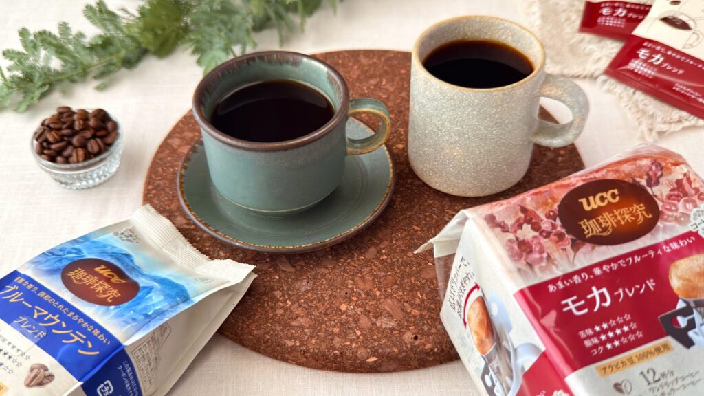 UCC_マグカップに注いだ「UCC 珈琲探究 炒り豆 ブルーマウンテンブレンド 140g（豆）」と「UCC 珈琲探究 ワンドリップコーヒー モカブレンド 12杯分」がテーブルの上に置いてある様子