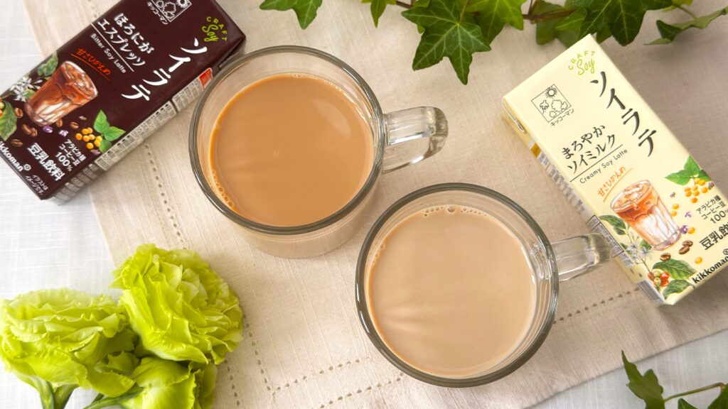 キッコーマン豆乳_グラスにはいった「クラフトソイ ソイラテ まろやかソイミルク」と「クラフトソイ ソイラテ ほろにがエスプレッソ」とパッケージがテーブルに置いてある様子