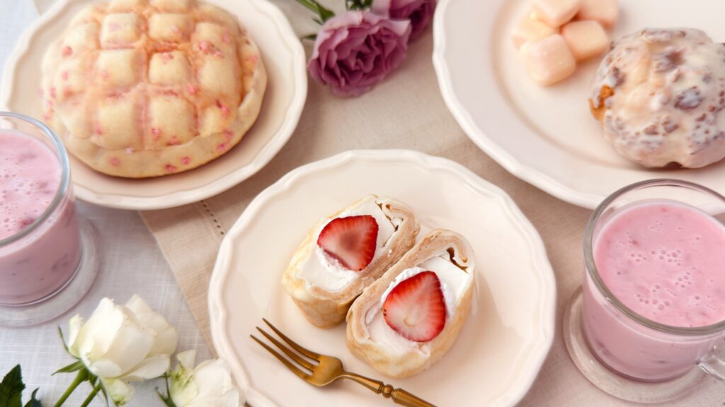 ファミリーマート_「ファミマの白をまとったいちご狩り®」の「ザクザク食感 いちごのクッキーシュー」や「ミルク楽しむいちごミルク」などがテーブルに並んでいる様子