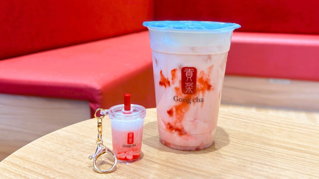 ゴンチャ_「いちご杏仁 ミルクティー」とミニチュアキーホルダーがテーブルに置いてある様子