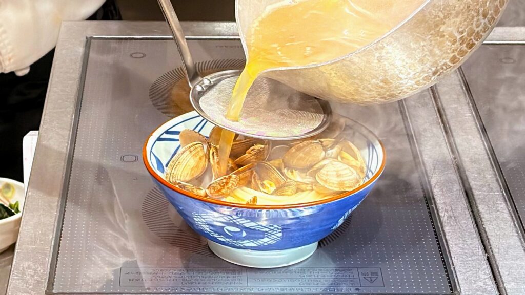 丸亀製麺_「山盛りあさりうどん」のつゆを注いでいる様子