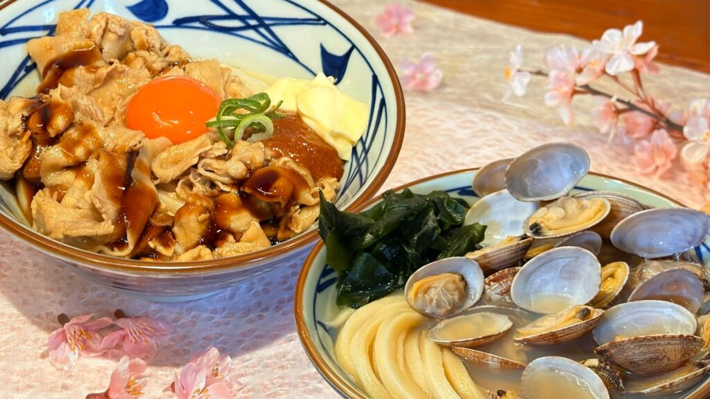 丸亀製麺_桜に囲まれた「こく旨豚玉ぶっかけうどん」と「山盛りあさりうどん」