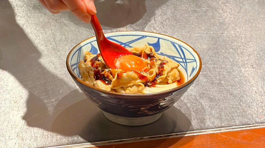 丸亀製麺_「こく旨豚玉ぶっかけうどん」に卵黄をのせている様子