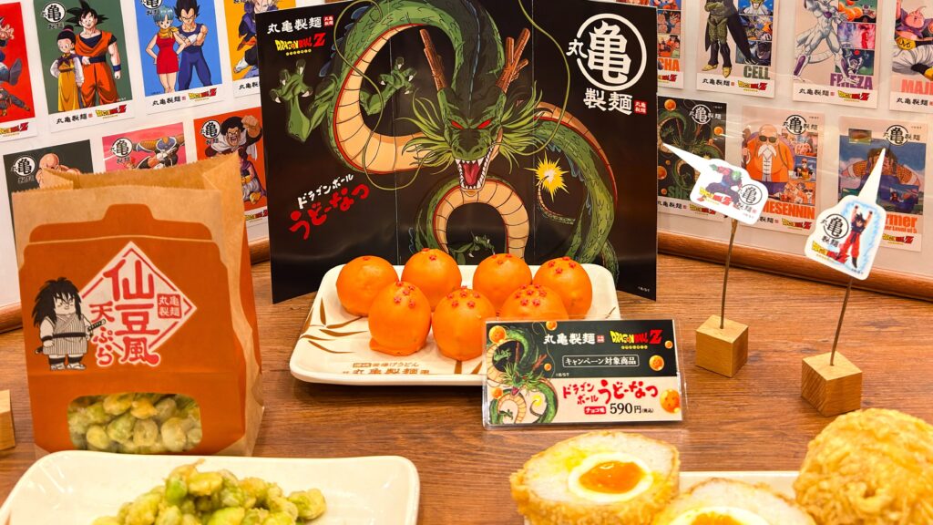 丸亀製麺_ドラゴンボールZコラボの「ドラゴンボールうどーなつ（チョコ味）」や「元気玉おむすび半熟卵入り」「仙豆風天ぷら」が並んでいる様子