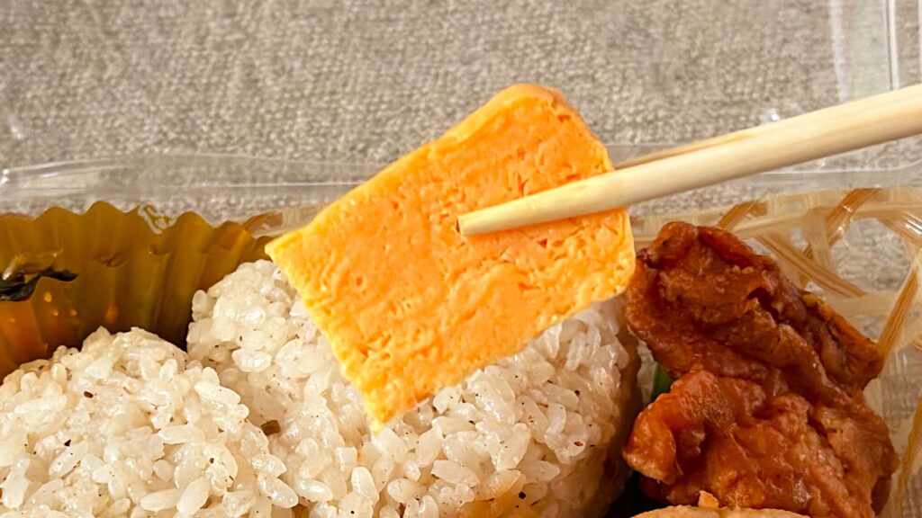 やまや_「やまや うまだしおにぎりセット」のたまごを箸で持っている様子