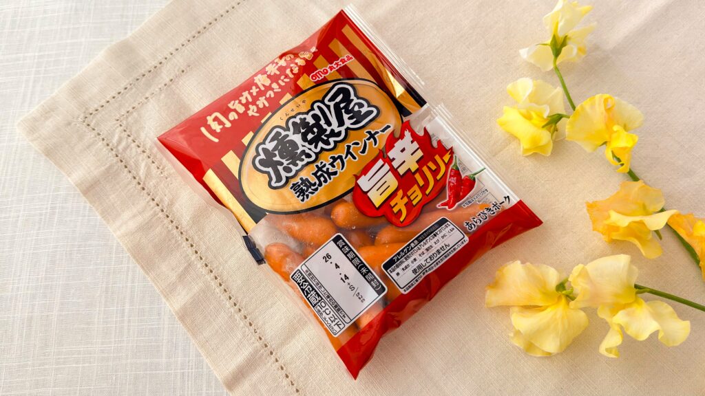 丸大食品_「燻製屋熟成ウインナー 旨辛チョリソー」のパッケージとお花が並んでいる様子