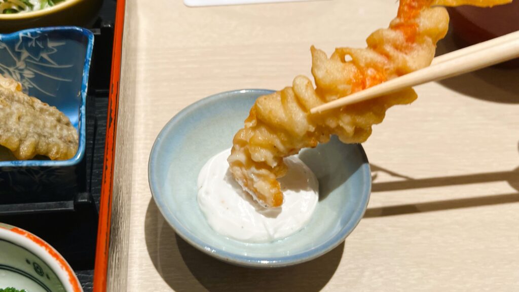 ファンケル_創作料理 FANCL 令和本膳「美腸活弁当」の海老と季節野菜の玄米粉天婦羅の海老天をヨーグルトサワークリームにつけている様子
