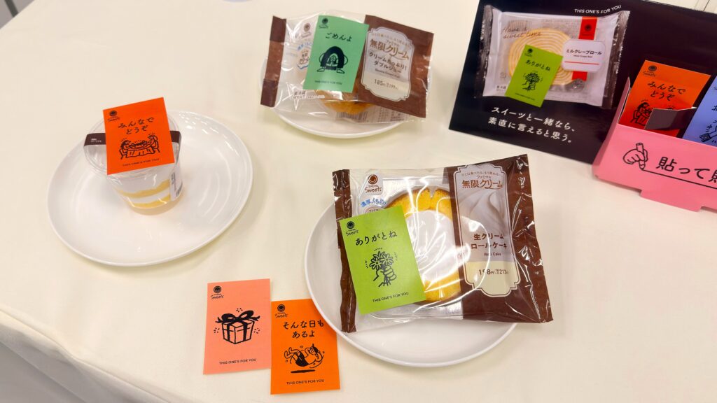 ファミリーマート_展示された「クリームたっぷり！ダブルシュー」や「生クリームロールケーキ」、「ほぼクリームのケーキ」のパッケージとメッセージカード